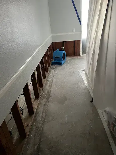 Hallway with flood-cut drywall and an air mover drying the bare slab
