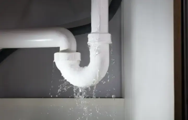 Water spraying from a failed joint on a pipe under a sink
